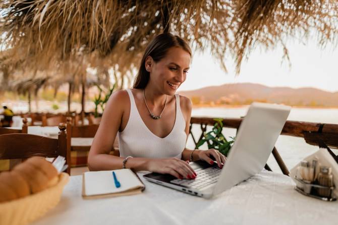 A woman working on a laptop in a beach location.