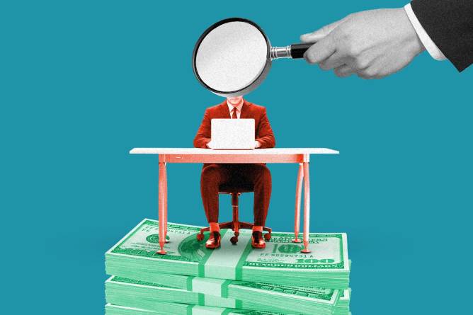 An employee at a desk on a stack of money under a magnifying glass