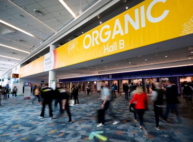 People walk inside a convention center past a sign that says "Organic."