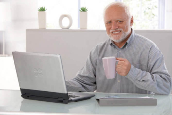 Man with bear smiling up from his computer, holding a mug