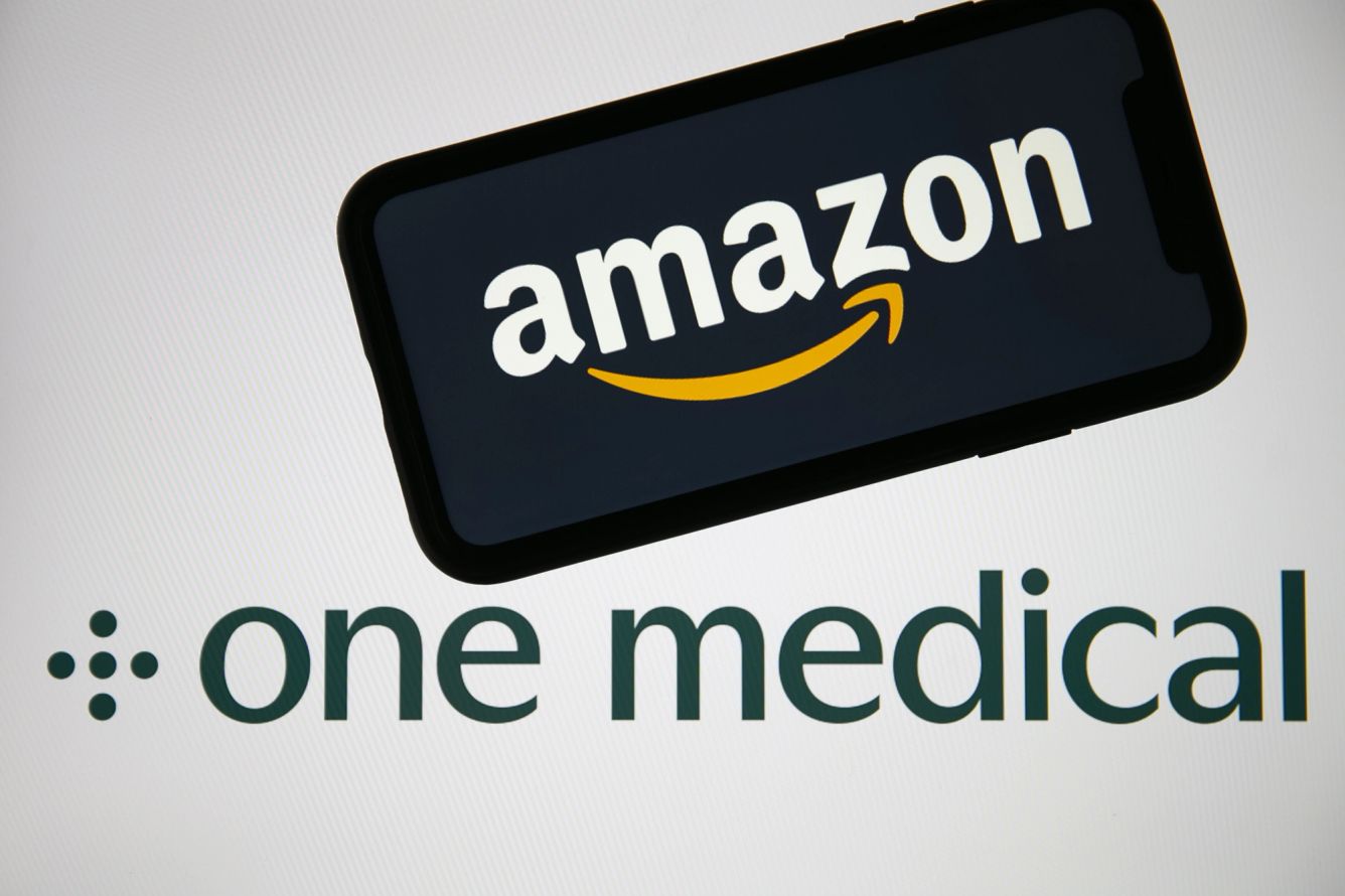 A phone showing Amazon's logo is pictured on top of the logo for One Medical.