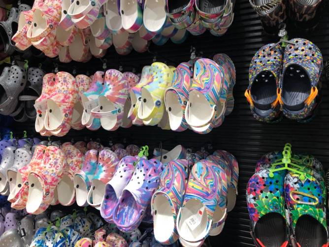 Multicolored Crocs hanging on a wall rack in a store.