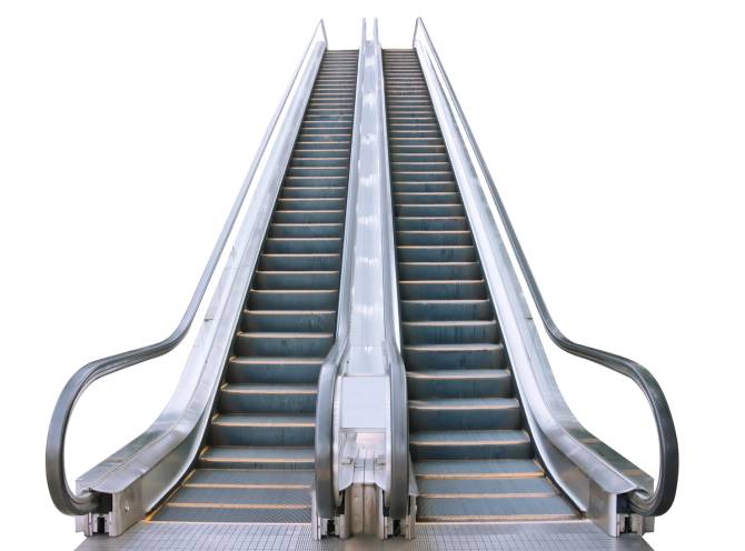 A photograph of escalators with a neutral white background. 