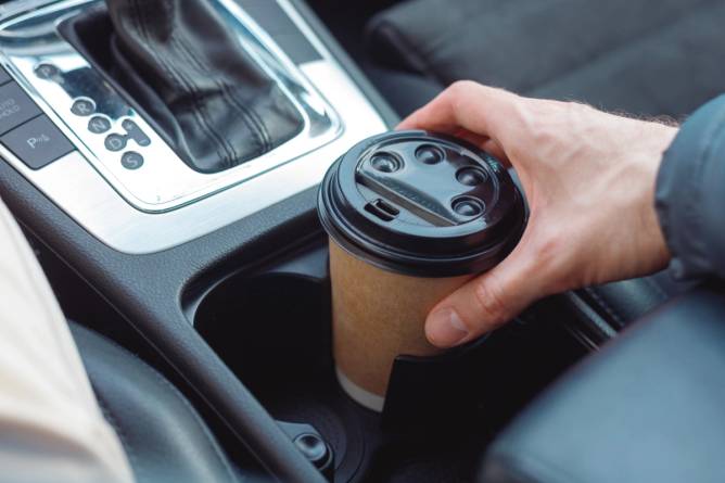 a hand putting a coffee cup in a car cupholder