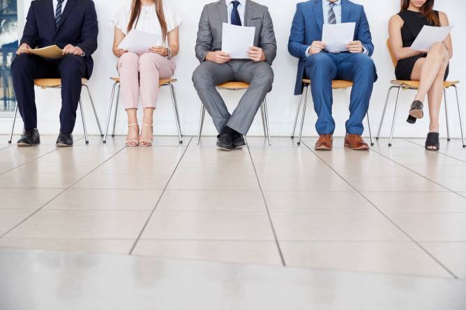 Five people sitting in chairs holding papers waiting to be interviewed.