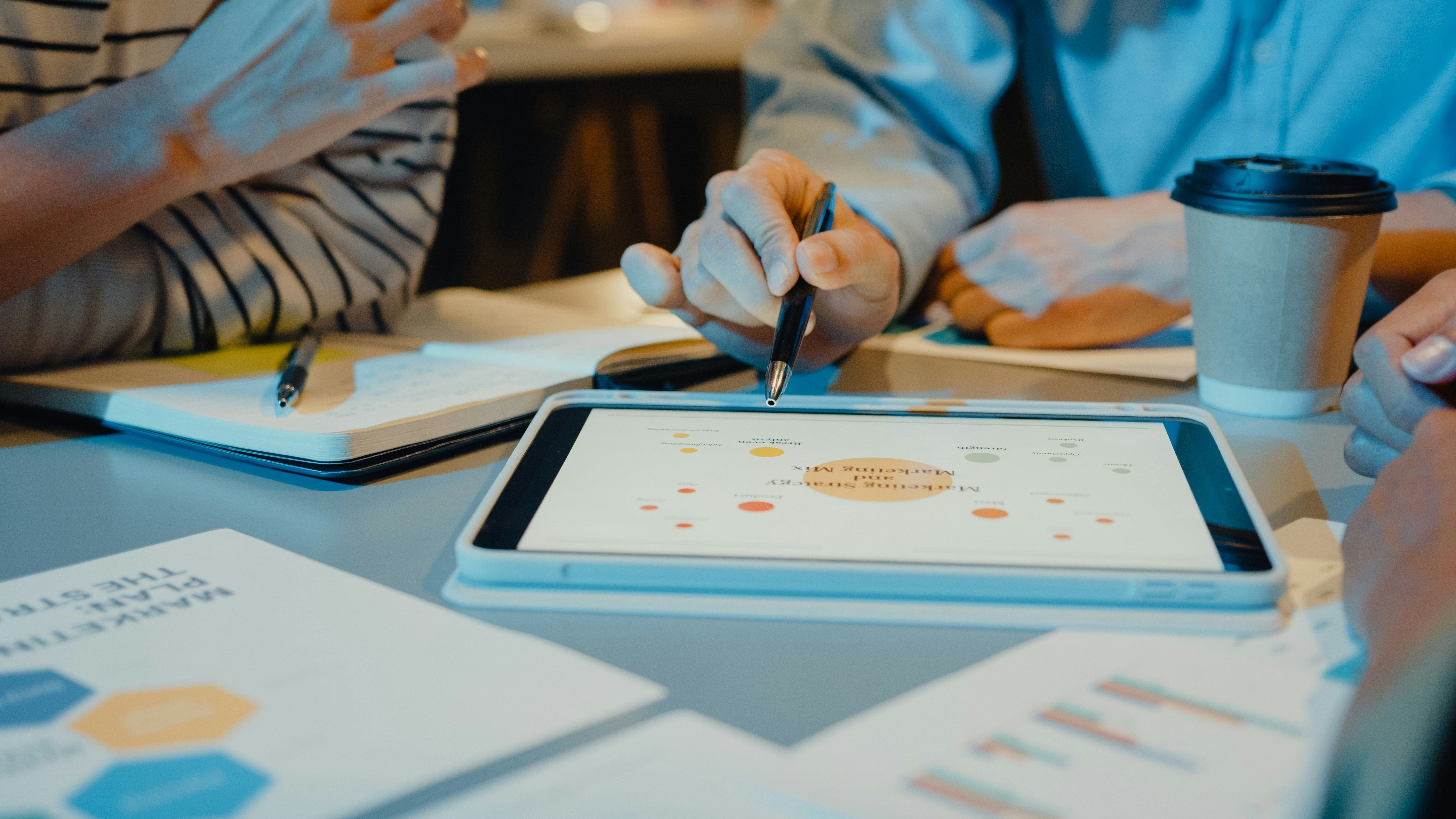 Two people sitting at desk looking at report on a tablet and using a stylus.