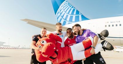 Wrexham AFC players holding the Wrexham mascot in their arms in front of a United Airlines airplane