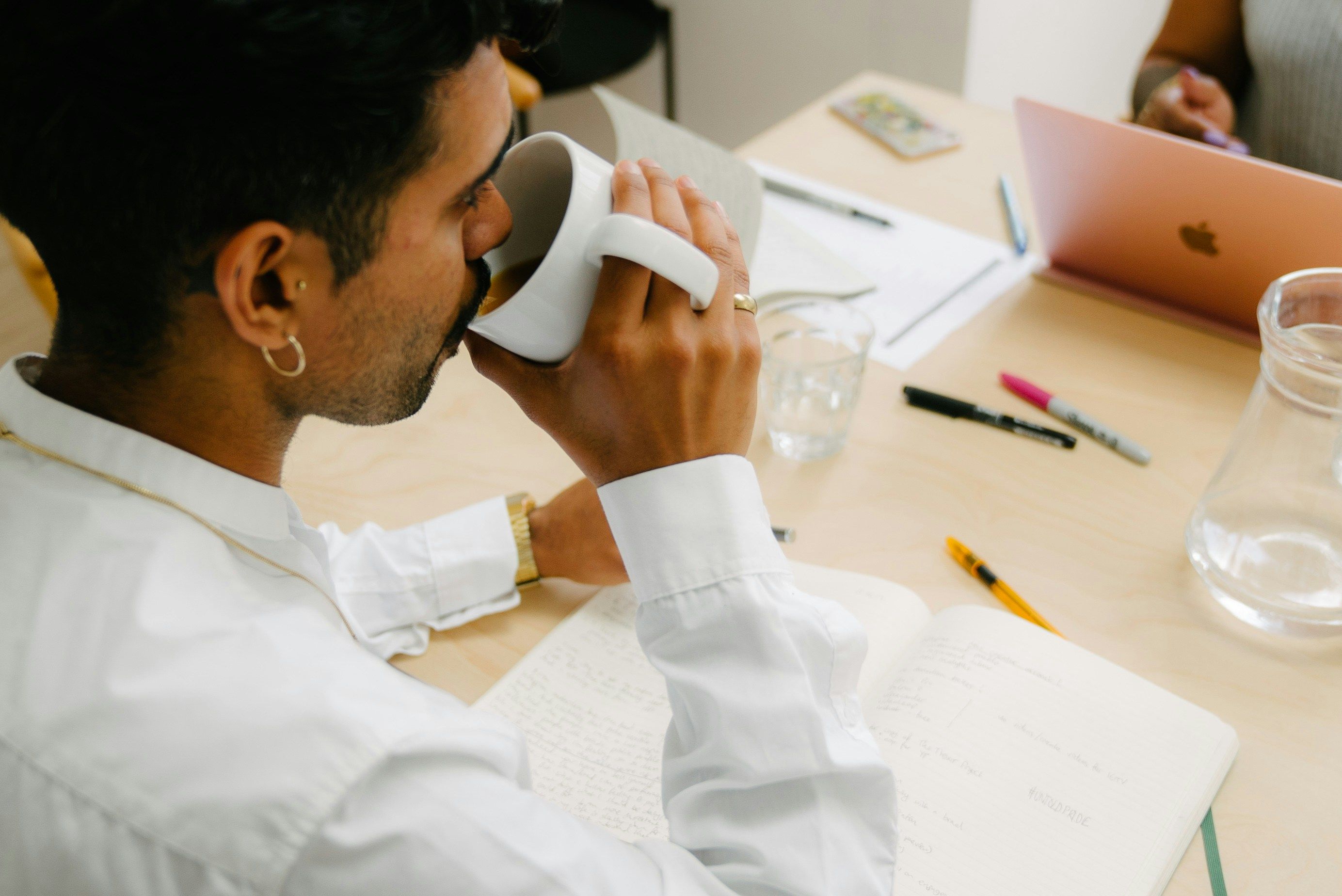 Side view of man sipping from mug at desk with coworkers.