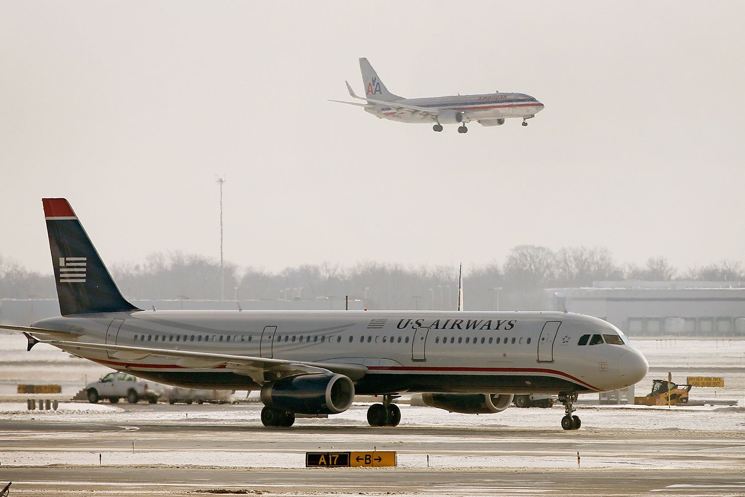 A United Airways plane sits on the tarmac while an American Airline plane is seen landing in the background