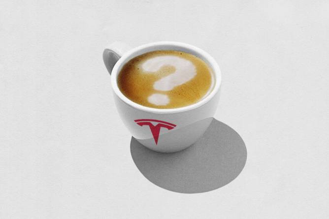 A coffee mug with the Tesla logo on it filled with a drink with a question mark in the milk