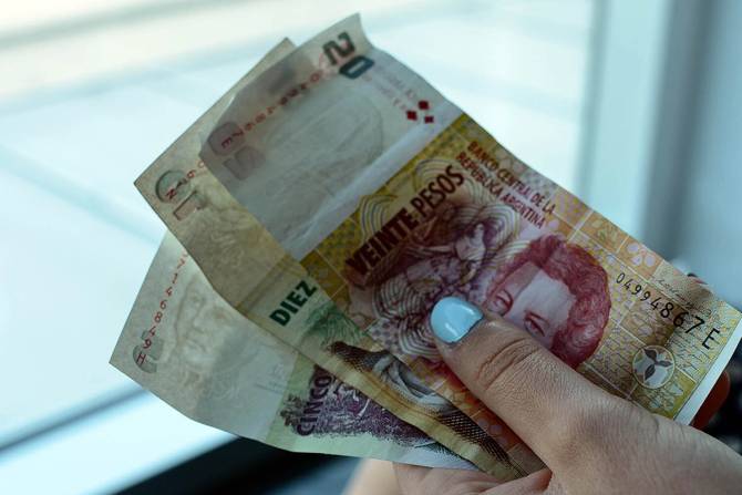 A hand holding Argentina's currency, the peso