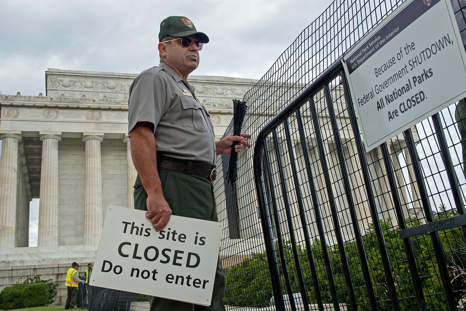 A government worker stands at a fence besides the Supreme Court, holding a sign that reads, 'This site is closed, do not enter'