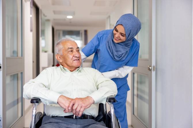 A Muslim nurse wearing a hijab takes care of an older patient in a wheelchair