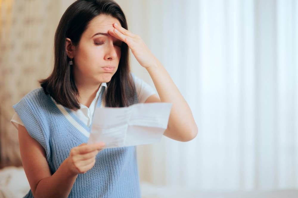 A woman brings her hand to her head as she looks at a document.
