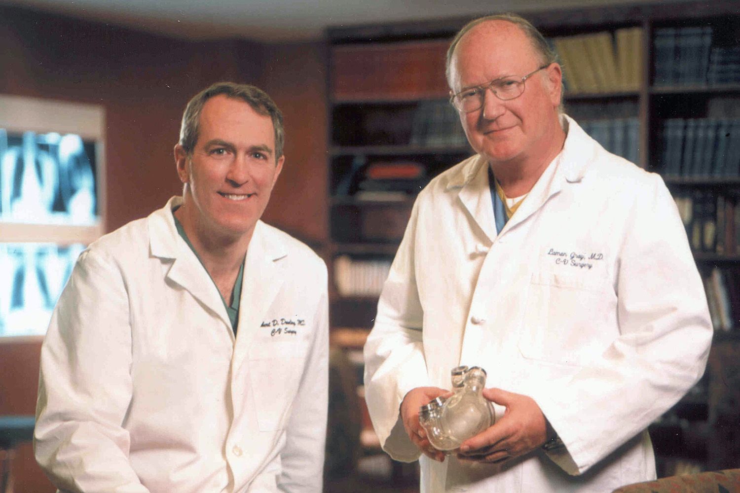 Two middle aged white men with lab coats stand holding a glass object in medical office.