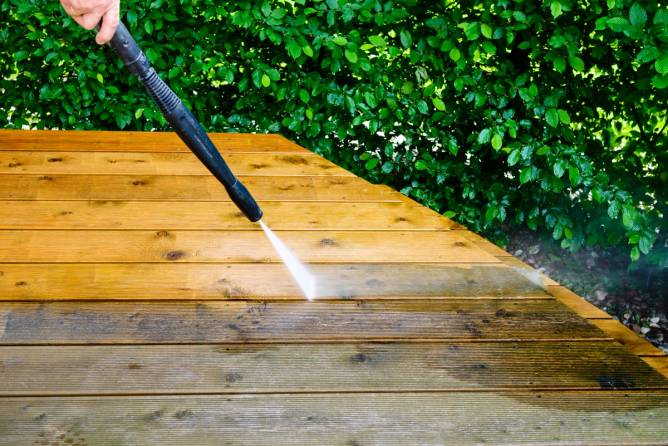 Image of a person power washing a deck. 