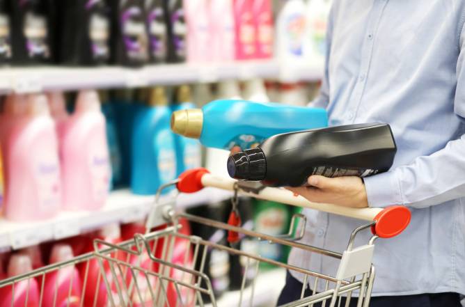 Shopper in a grocery store aisle comparing bottles of detergent