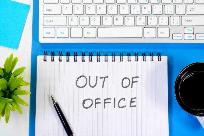 A notepad under a keyboard reads "out of office."