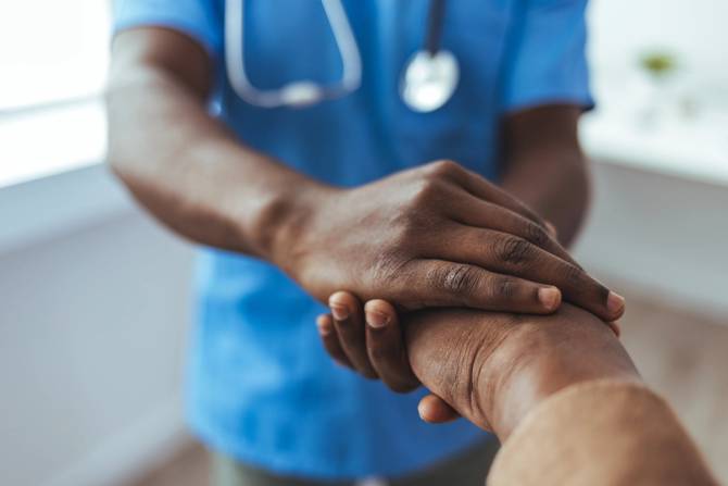 A doctor holds an elderly patient's hand.