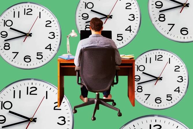 A rear view of a man sitting at desk working at computer surrounded by giant clocks.