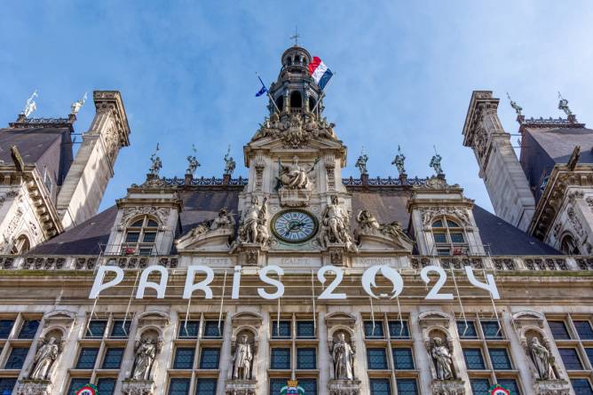 a building in Paris promoting Paris 2024 Olympic Games on the facade, with a French flag flying above 