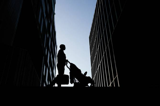 A person walks with a stroller against a blue sky.