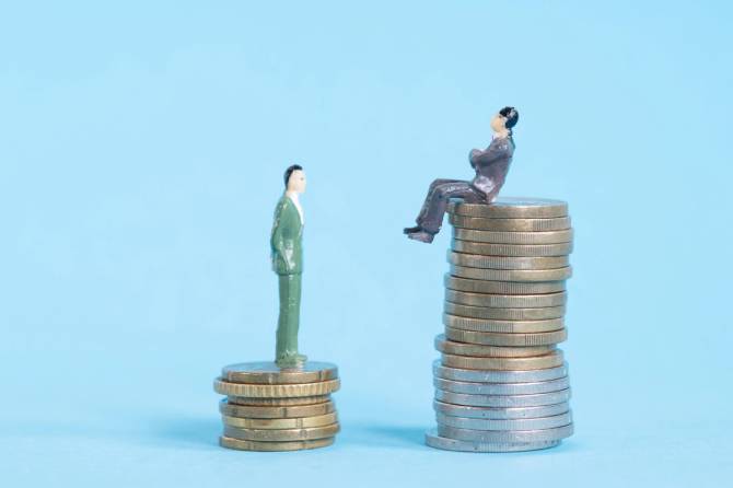 Stacks of coins with a figurine standing on top of the little stack and a figuring sitting n the bigger stack in front of a blue background