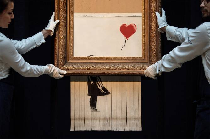 Sotheby's employees pose with 'Love is in the Bin' by British artist Banksy