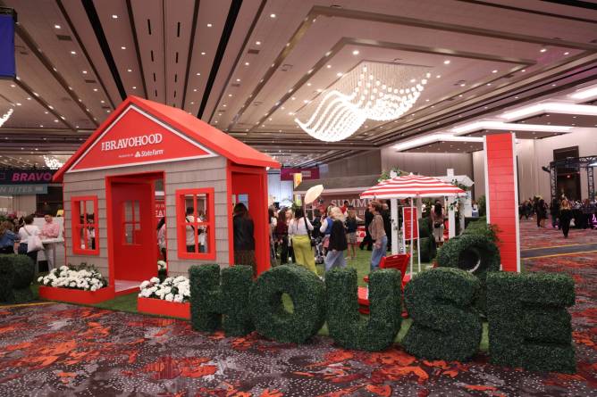 a branded facade of a home and a faux lawn promoting "The Bravohood" sponsored by State Farm on the ground at BravoCon in Las Vegas in 2023