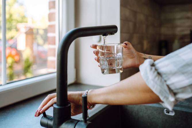 A person fills a glass of water from a sink.