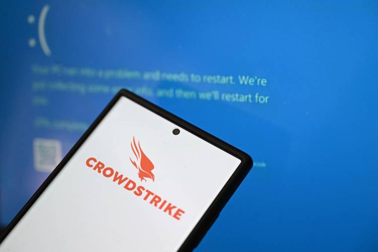 CrowdStrike logo on phone screen is displayed in front of Blue Screen of Death errors