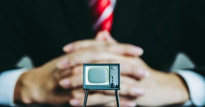 Closeup of a businessman’s suit folding his hands in front of a miniaturized retro TV