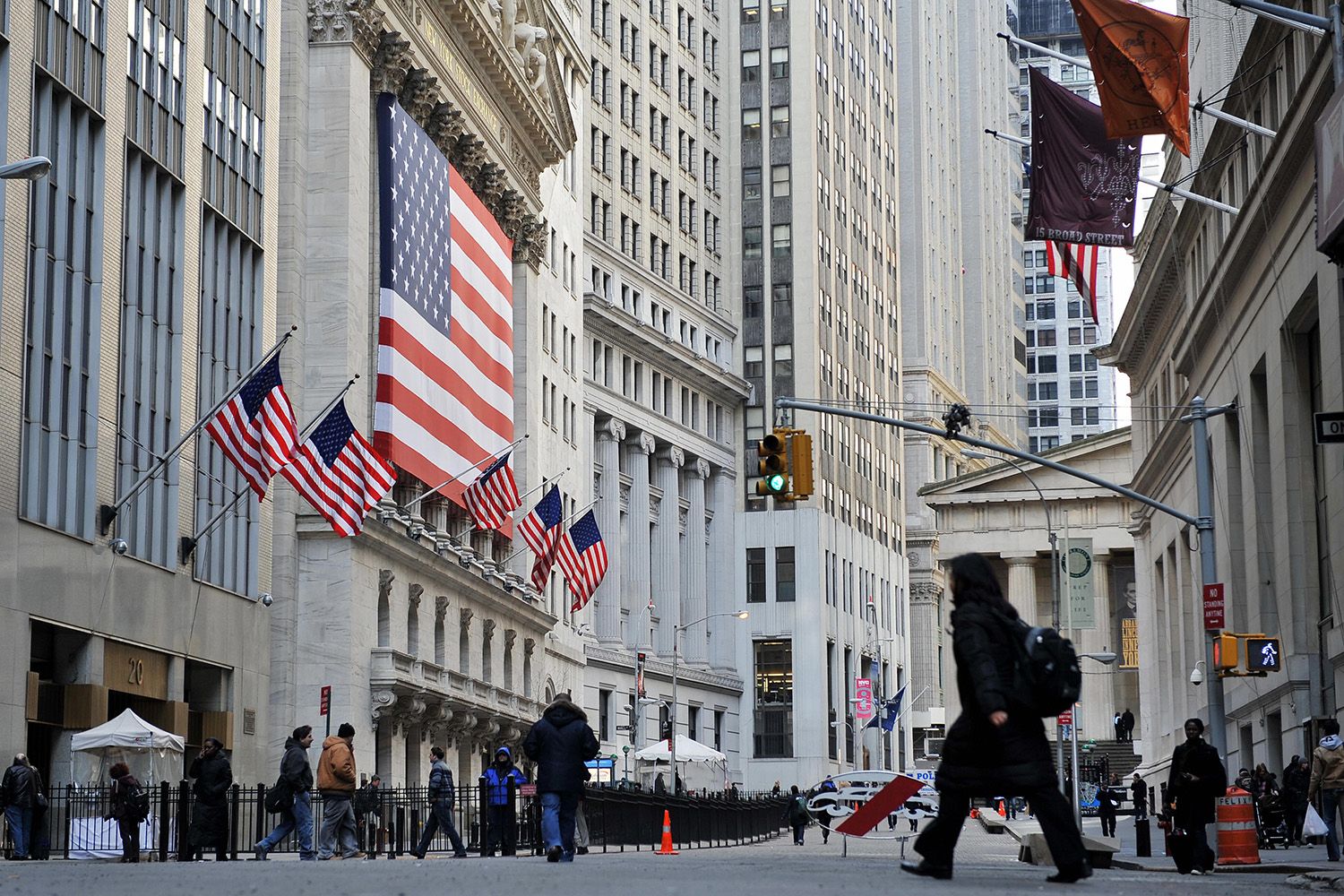 Street scape with minimal foot traffic, Wall Street in the financial district of New York City, American flag hangs in front of columned building.