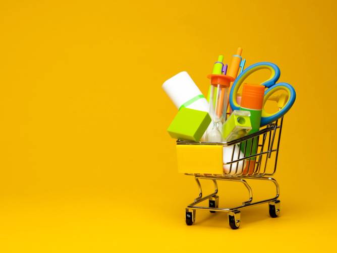 Back-to-school supplies including pens and scissors in a miniature shopping cart. 