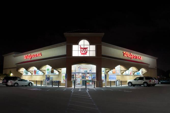 A photo of a Walgreens store at night, with lights illuminating two cars parked outside.