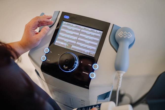 A healthcare professional’s hand interacting with the touchscreen of a medical device screen displaying treatment options.