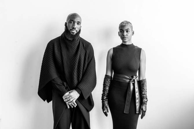 two people in black standing against white wall