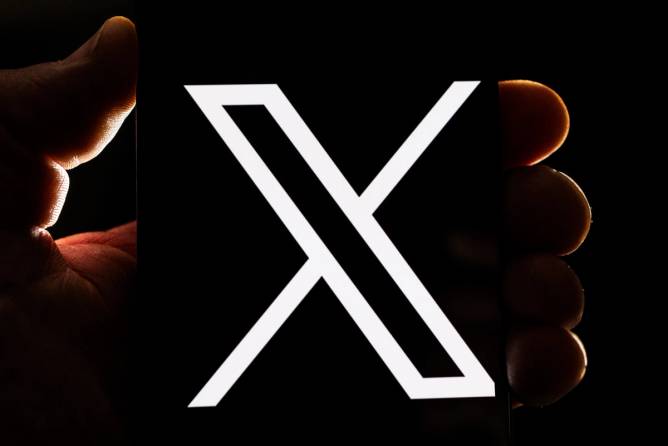 a hand clutches a phone with an X logo on the screen