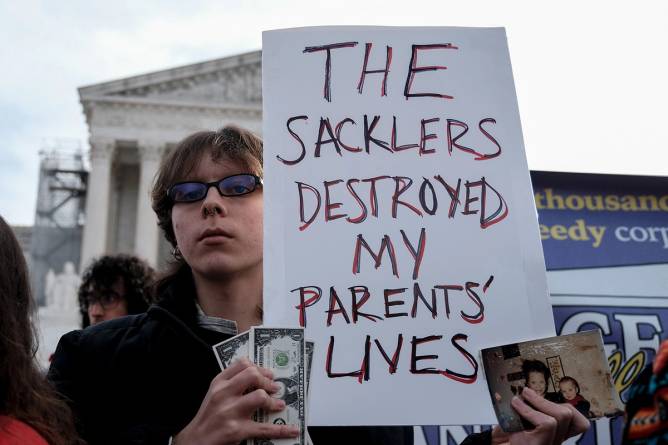 Photo of protestor holding sign that says “The Sacklers destroyed my parents lives.”