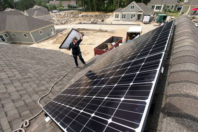 Jack Doherty, photovoltaic project manager for Revision Energy, carries a solar panel to the roof ridge of a home at OceanView at Falmouth