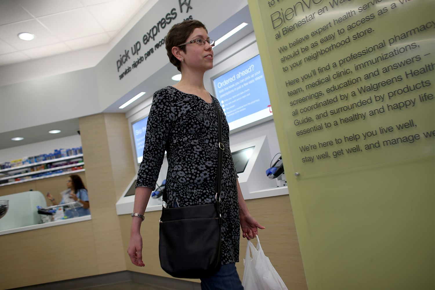 A woman is seen walking away from a pharmacy counter with a shopping bag in her left hand