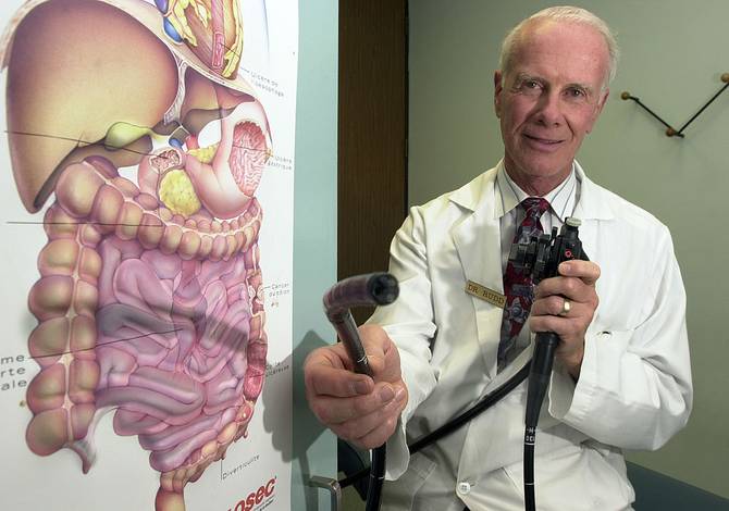 A doctor with a colonoscope stands beside a diagram of the digestive system