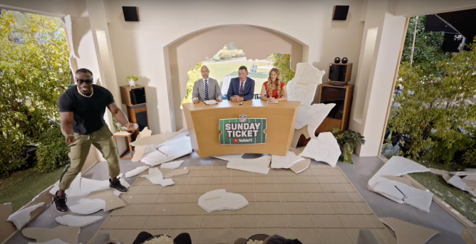 Shannon Sharpe appears in a campaign for NFL Sunday Ticket on YouTube in a fake room where TV announcers and a desk have just burst through a wall into a living room