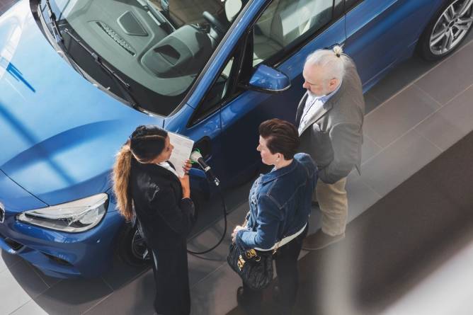 High angle of saleswoman speaking to customers next to a vehicle in a showroom