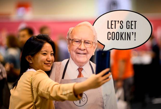 A woman poses for a picture with a cardboard cutout of Warren Buffett