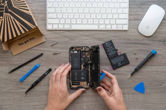 Photo of a woman's hands replacing a battery on an iPhone.