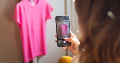 A woman holding her smartphone up to a pink t-shirt hanging on a rack to take a picture