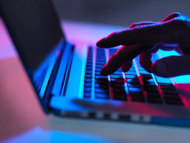 Silhouette of male hand typing on laptop keyboard at night.