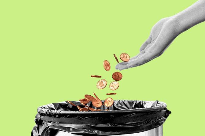 A hand throwing pennies into a trash can