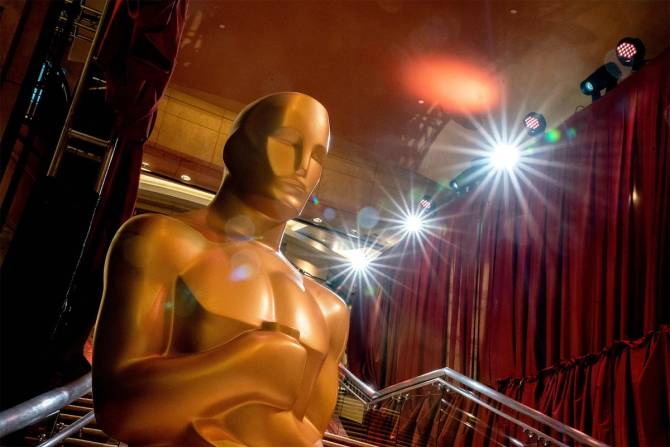 Oscars statue in front of red curtains.